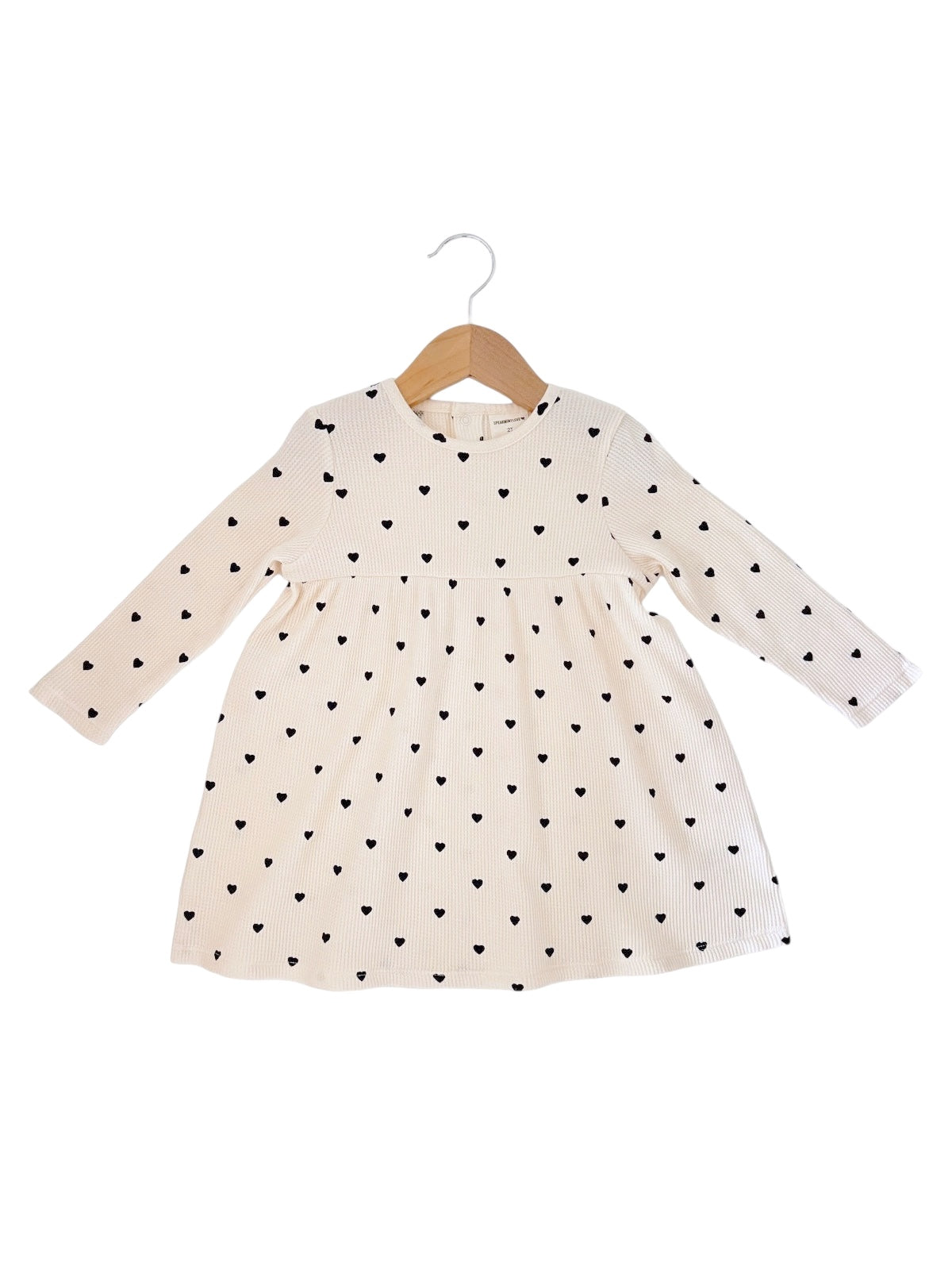 Cream dress with black heart pattern, long sleeves, and flared skirt, hanging on a wooden hanger.