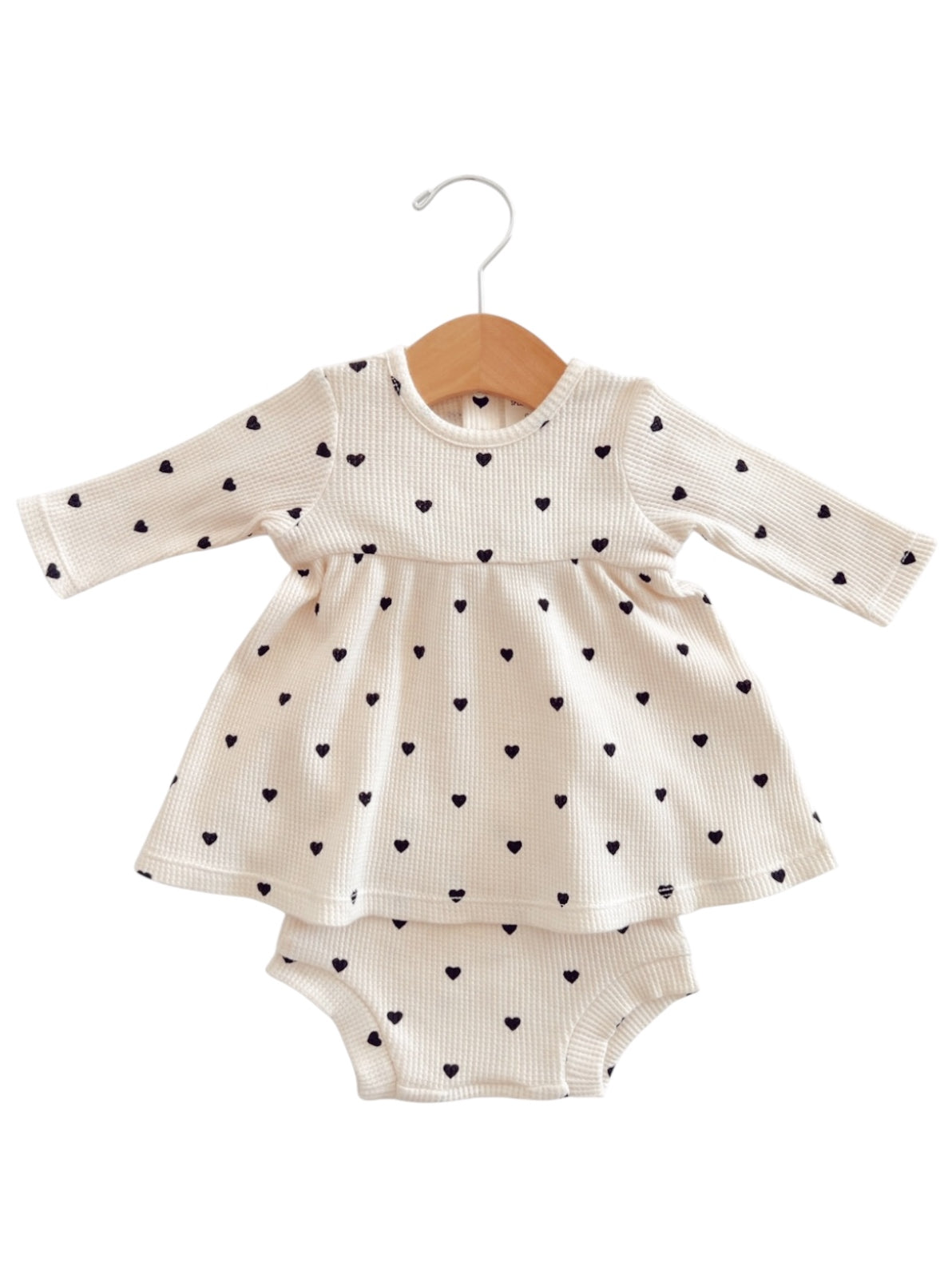 Cream dress with black heart patterns and matching romper underneath, hung on a wooden hanger.
