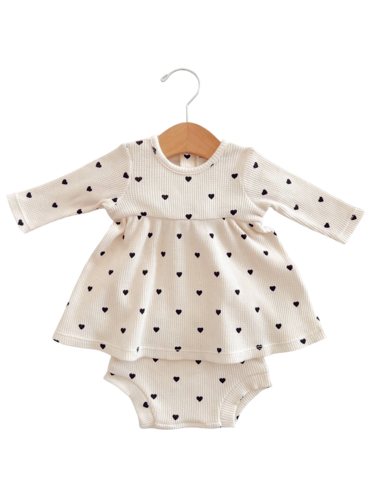 Cream dress with black heart patterns and matching romper underneath, hung on a wooden hanger.