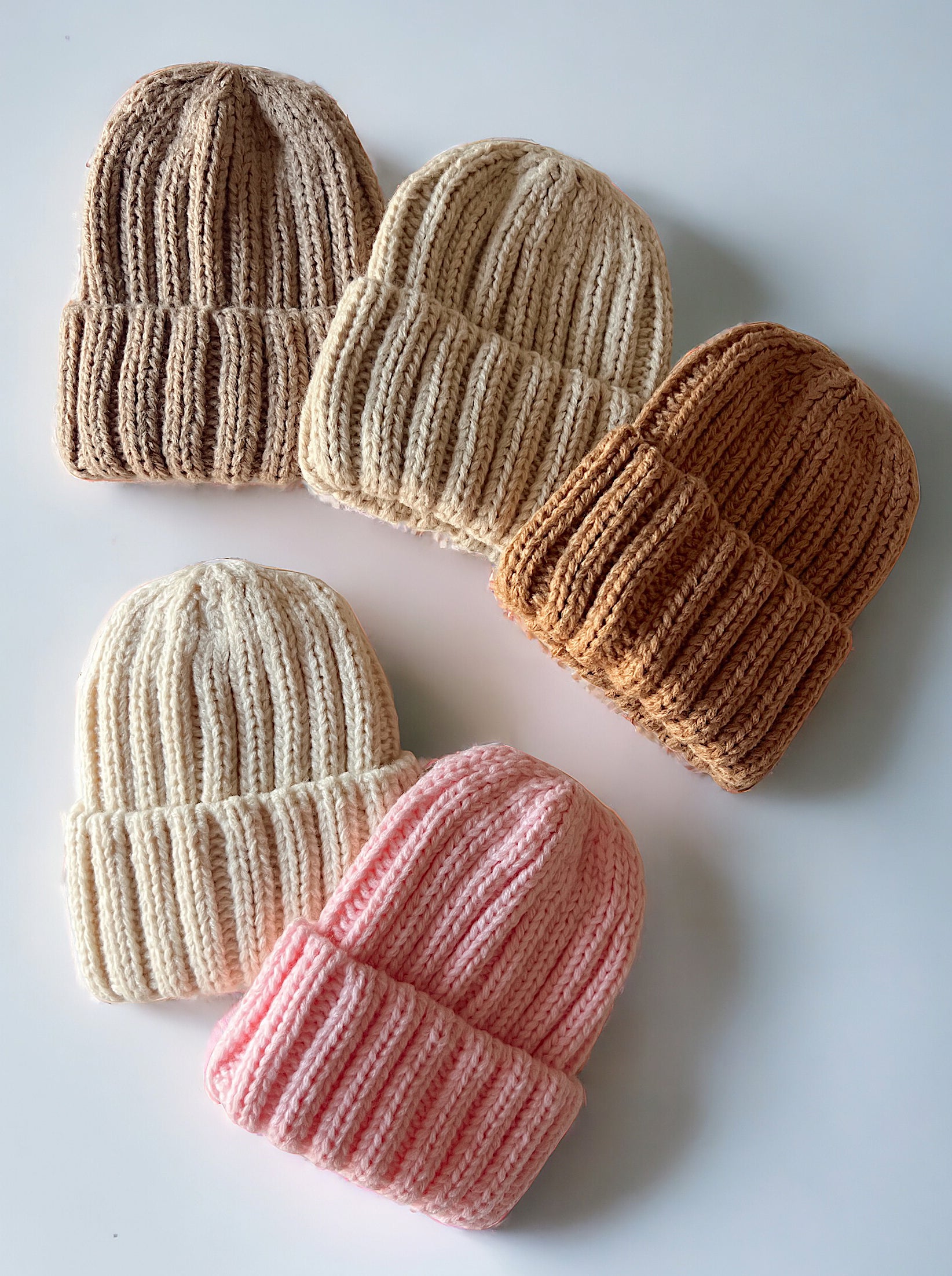 Five knitted beanies in various colors arranged on a white surface, showcasing their ribbed texture.