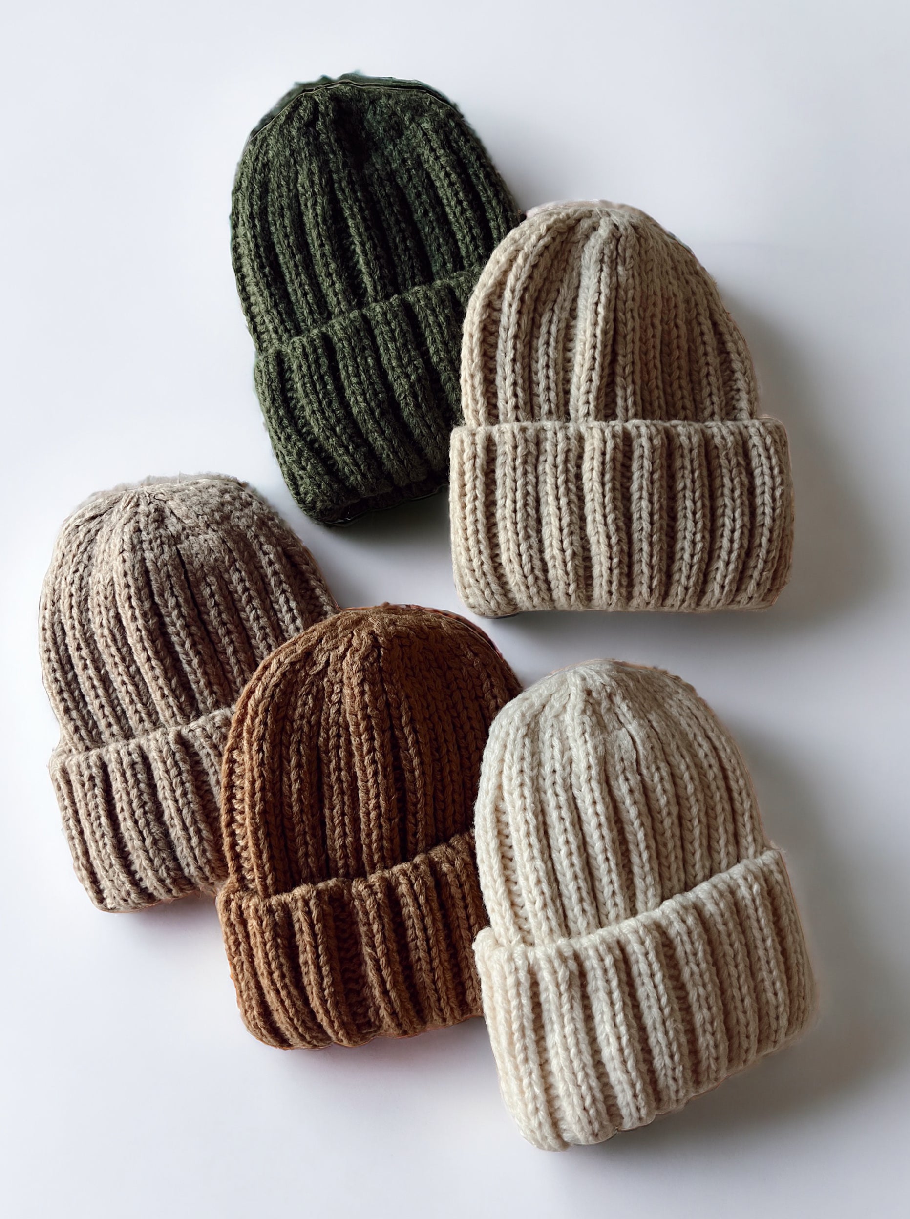 Six knitted beanies in green, beige, brown, and cream, arranged on a light background.