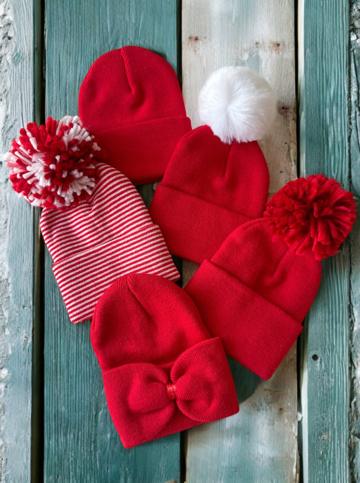 Five red beanies, including pom-pom styles and a bow design, arranged on a wooden surface.
