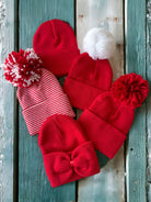 Collection of red winter hats, featuring different styles and pom-poms, on a rustic wooden background.