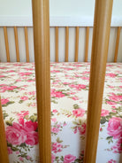 A wooden crib with vertical bars and a floral-patterned mattress featuring pink roses.
