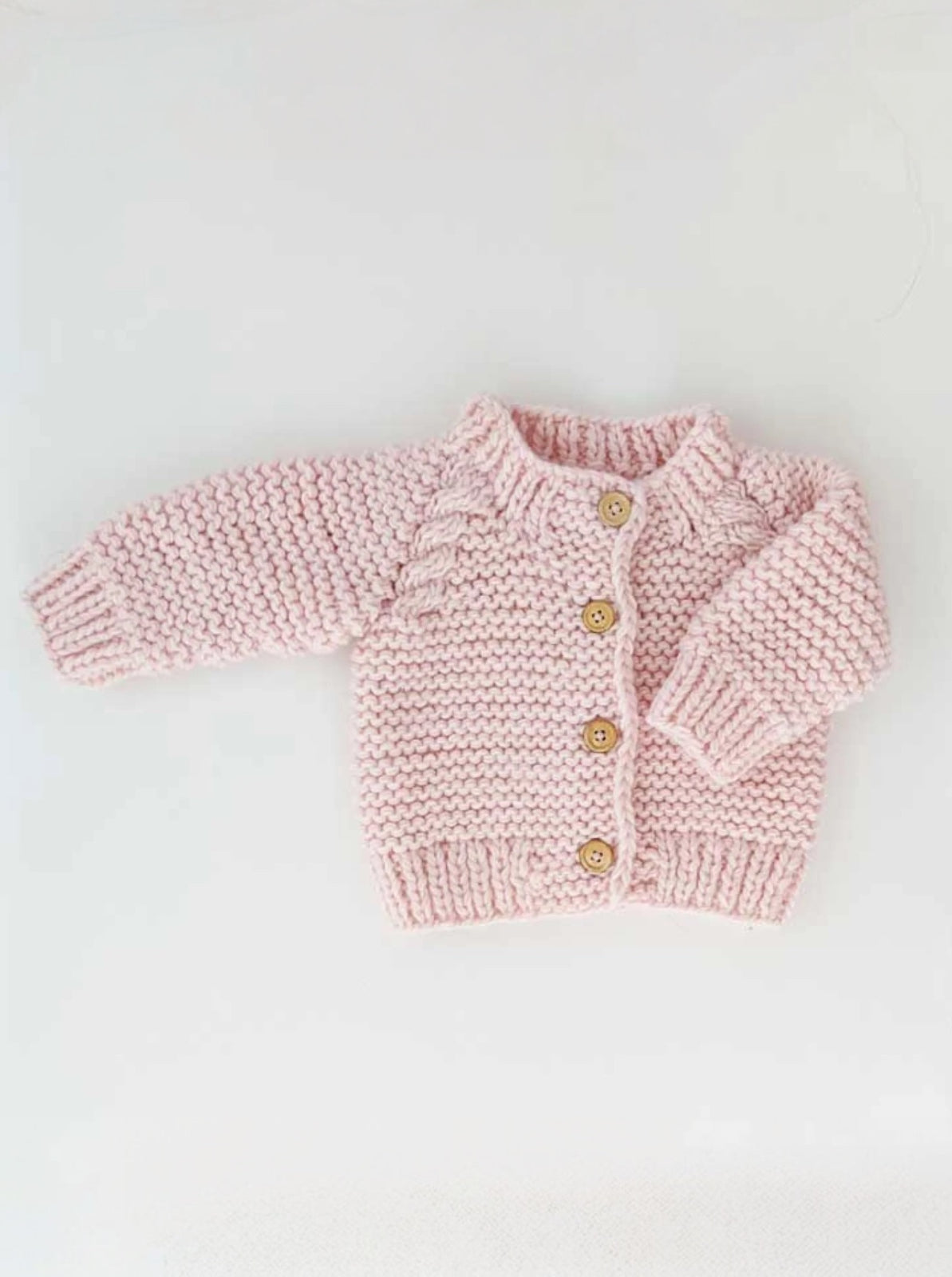 Baby pink knitted cardigan with wooden buttons on a white background.