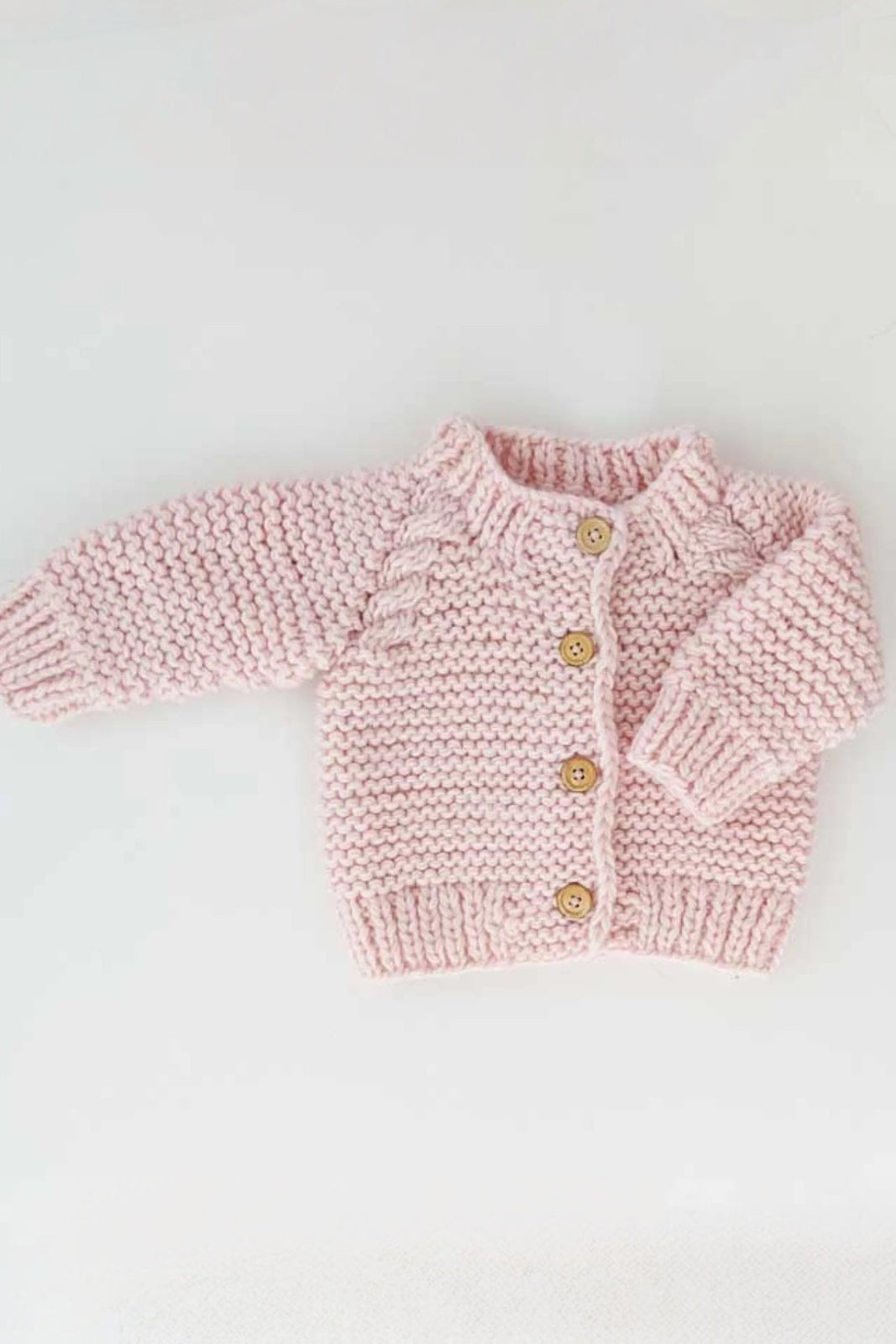 Baby pink knitted cardigan with wooden buttons on a white background.