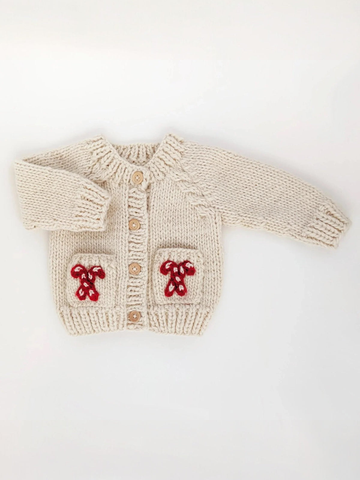 Knitted cream-colored baby cardigan with red embellishments and wooden buttons, displayed flat on a white background.