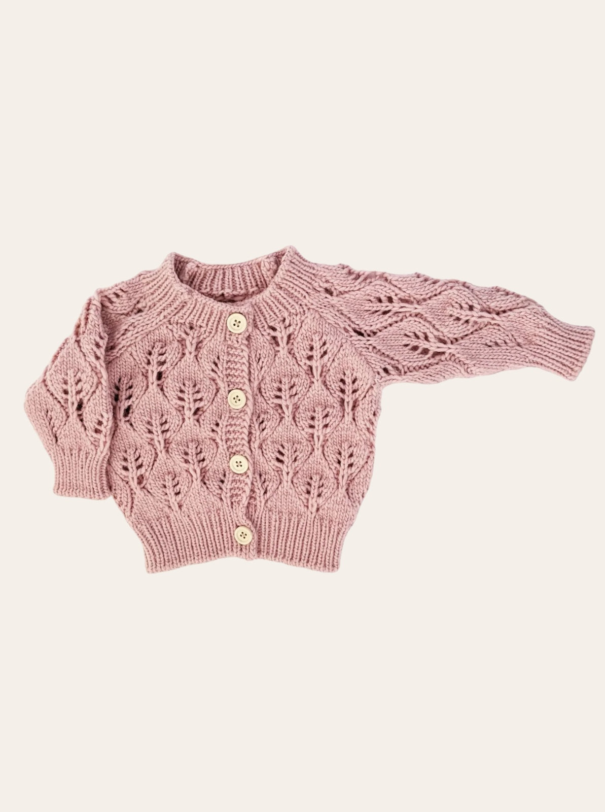 Knitted pink cardigan with leaf patterns and wooden buttons, laid flat against a neutral background.