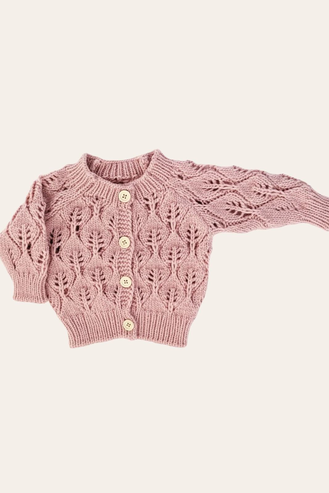 Knitted pink cardigan with leaf patterns and wooden buttons, laid flat against a neutral background.