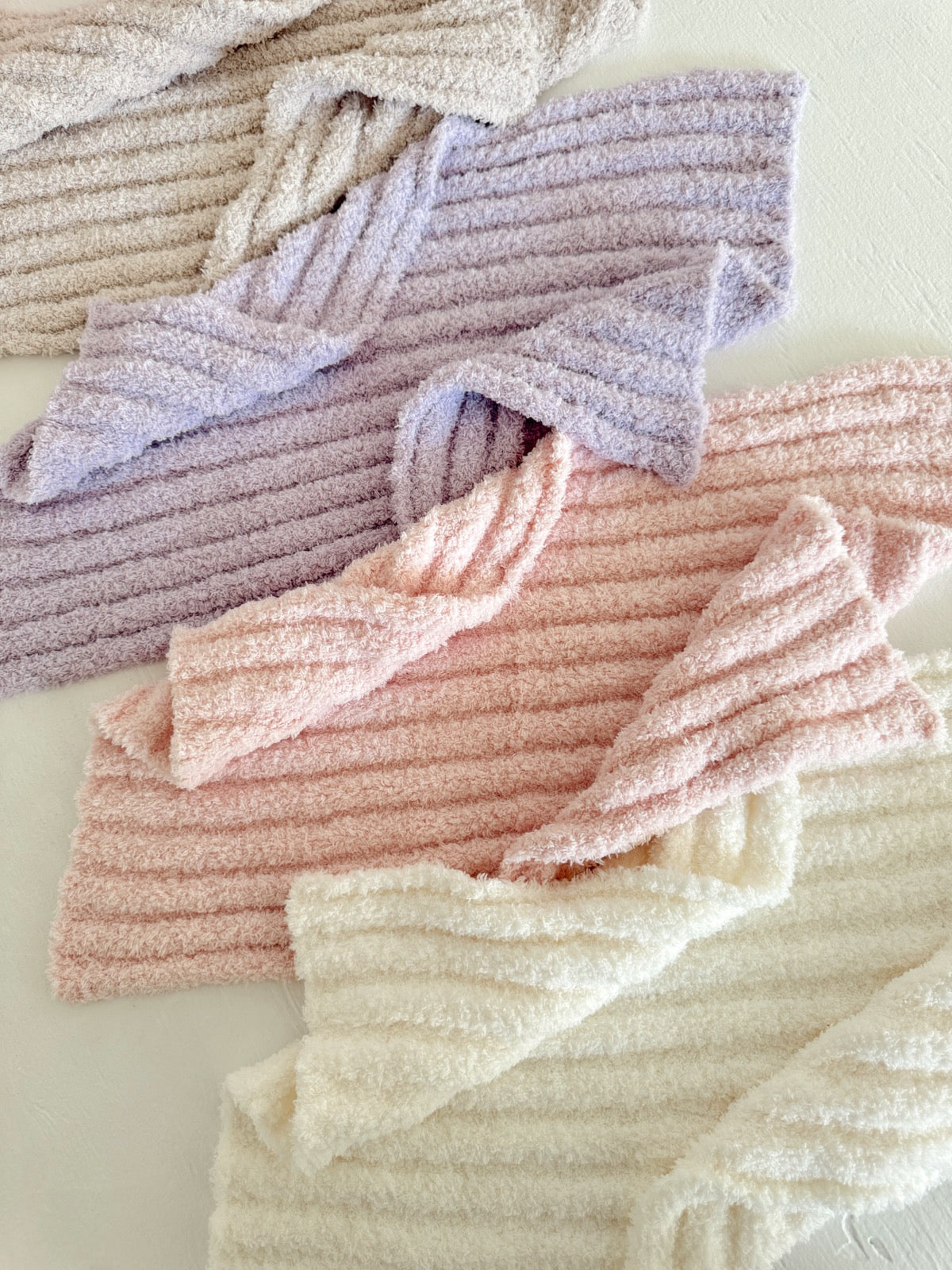 Various soft, textured towels in pastel colors: pink, lavender, cream, and beige arranged on a light surface.