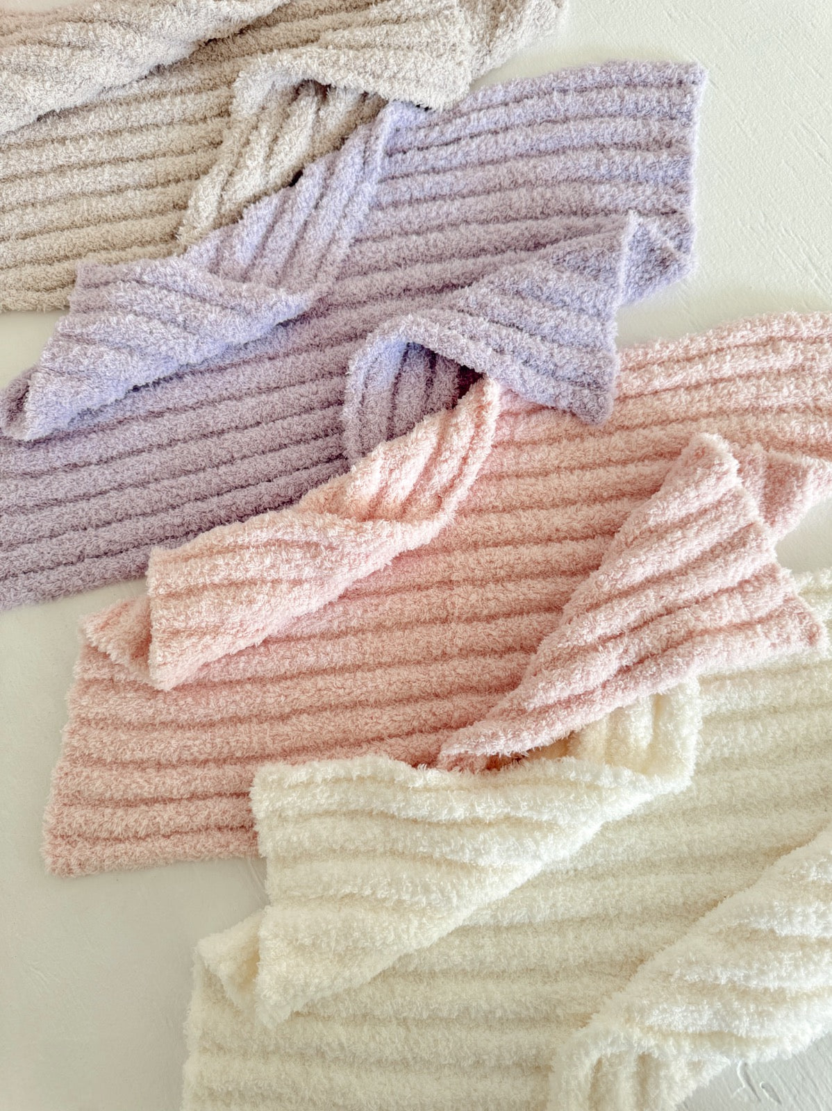Assorted plush, ribbed fabric pieces in pastel colors of lavender, pink, and white, arranged on a light background.