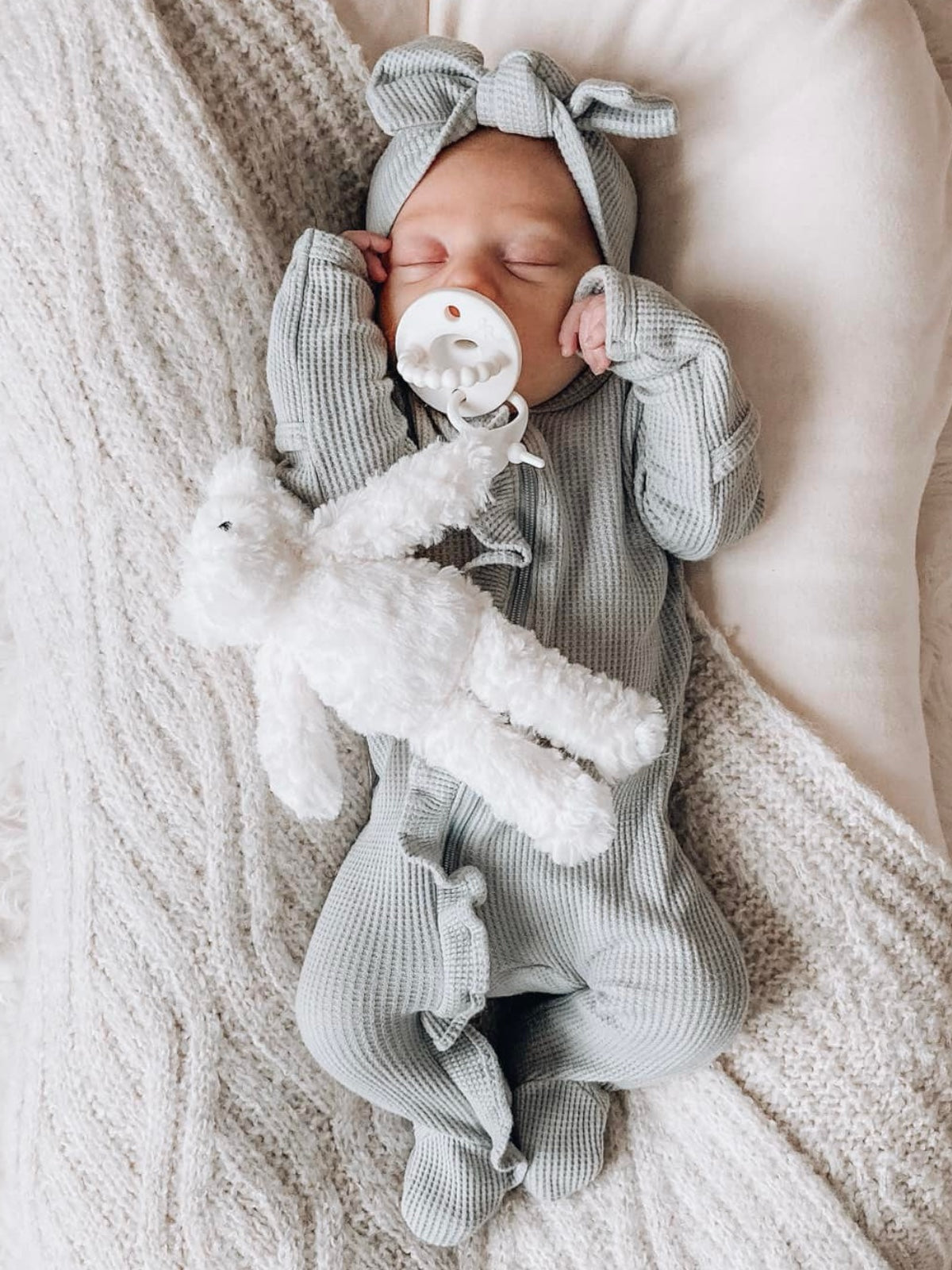 Sleeping baby in a gray outfit holding a stuffed toy, nestled in a cozy blanket.