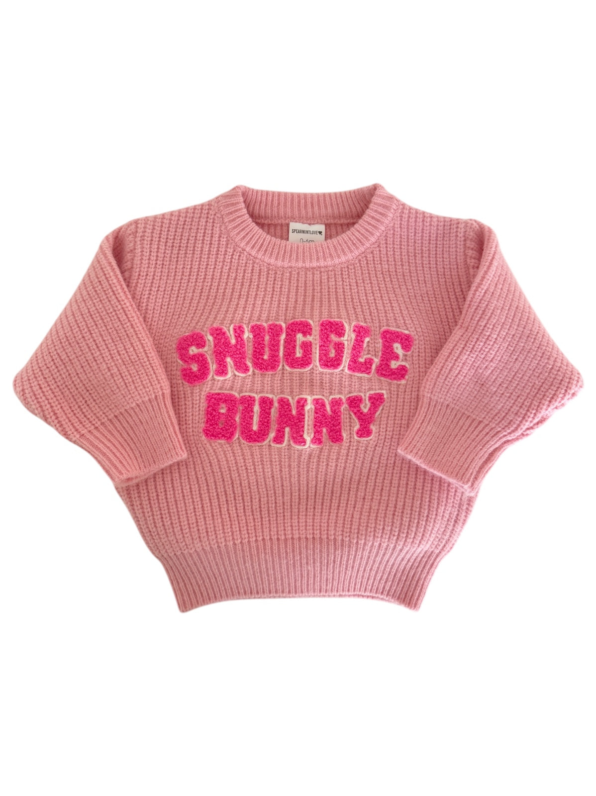 Pink knitted sweater with "Snuggle Bunny" in bold, sparkly letters on the front. Cozy and stylish apparel.