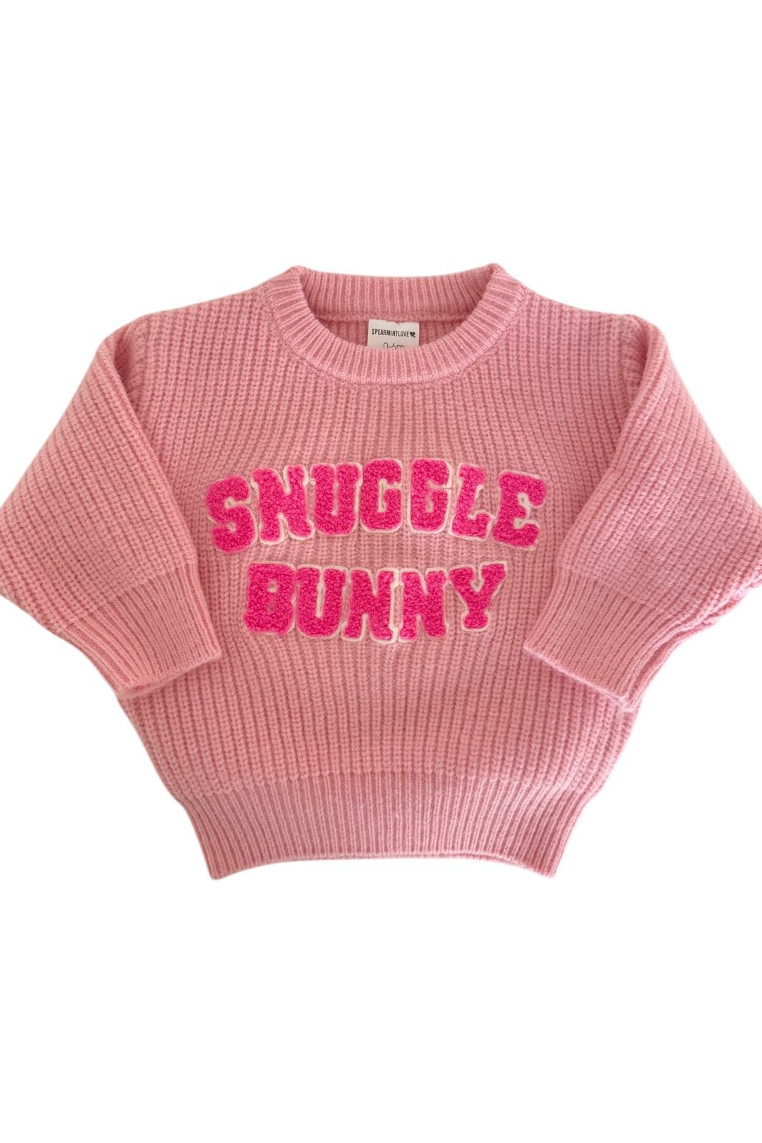 Pink knitted sweater with "Snuggle Bunny" in bold, sparkly letters on the front. Cozy and stylish apparel.