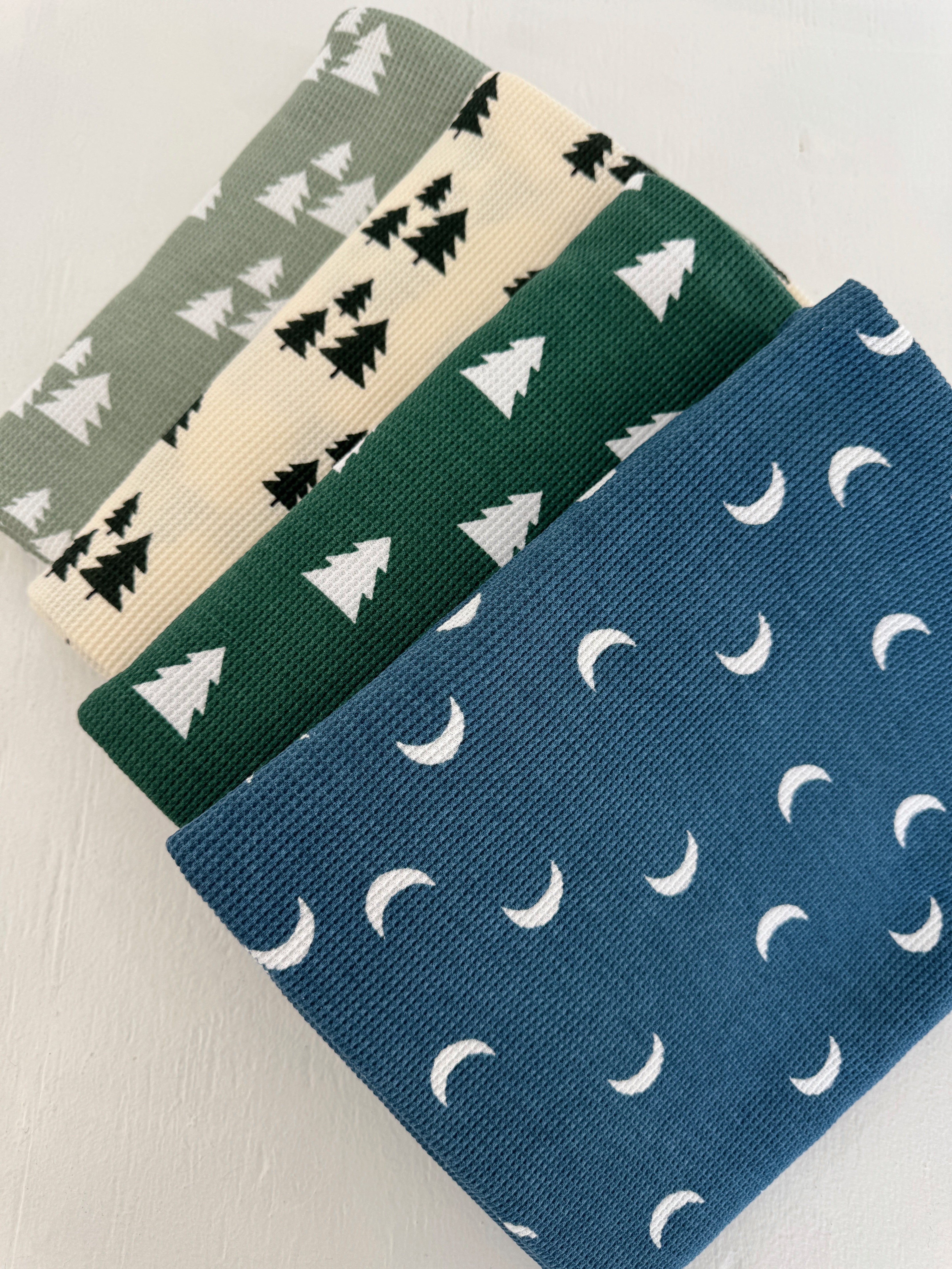 Four patterned fabrics in green, cream, and blue featuring trees and crescent moons stacked vertically.