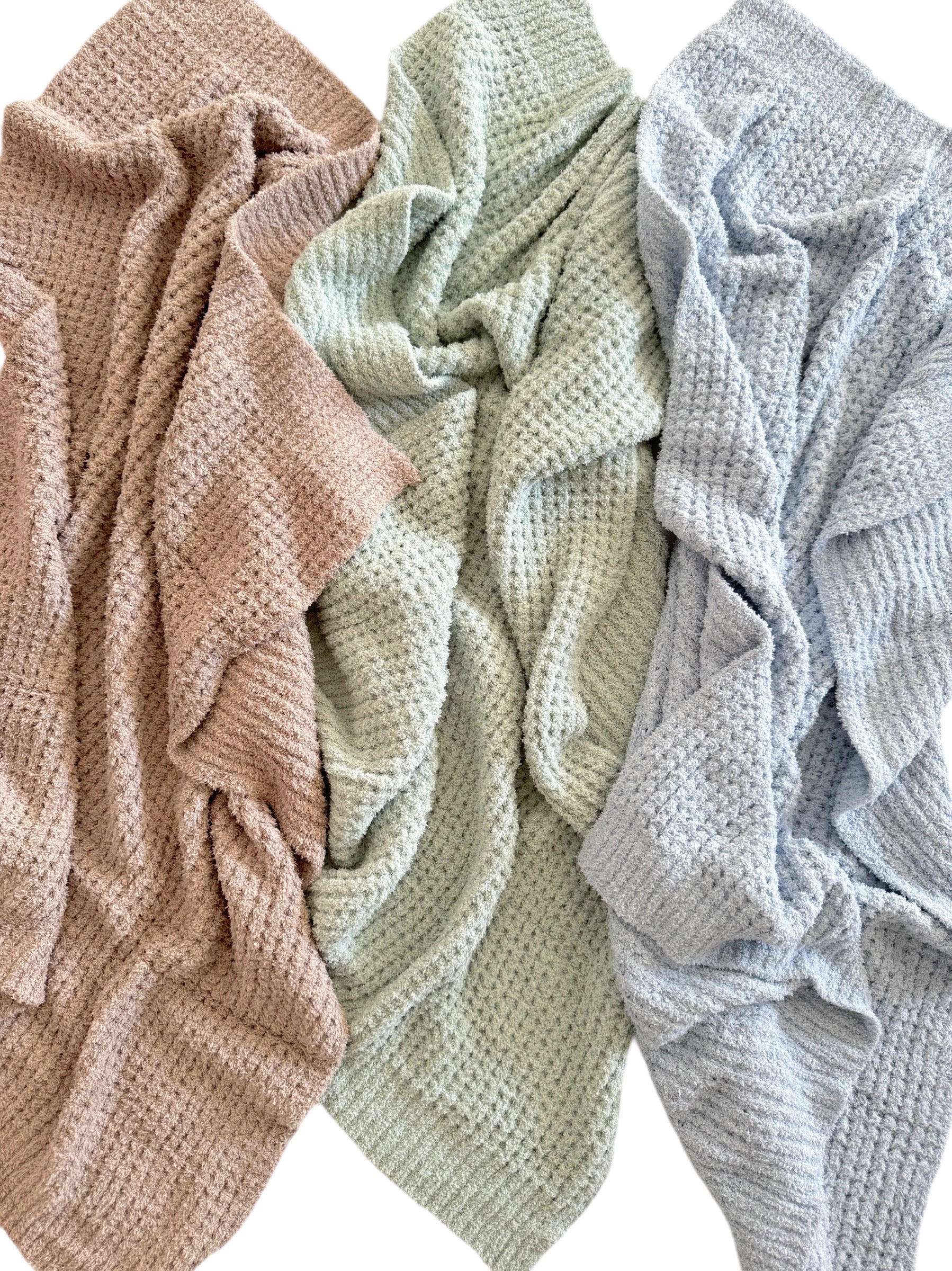 Three textured blankets in soft colors: pink, green, and blue, arranged in a cozy display.