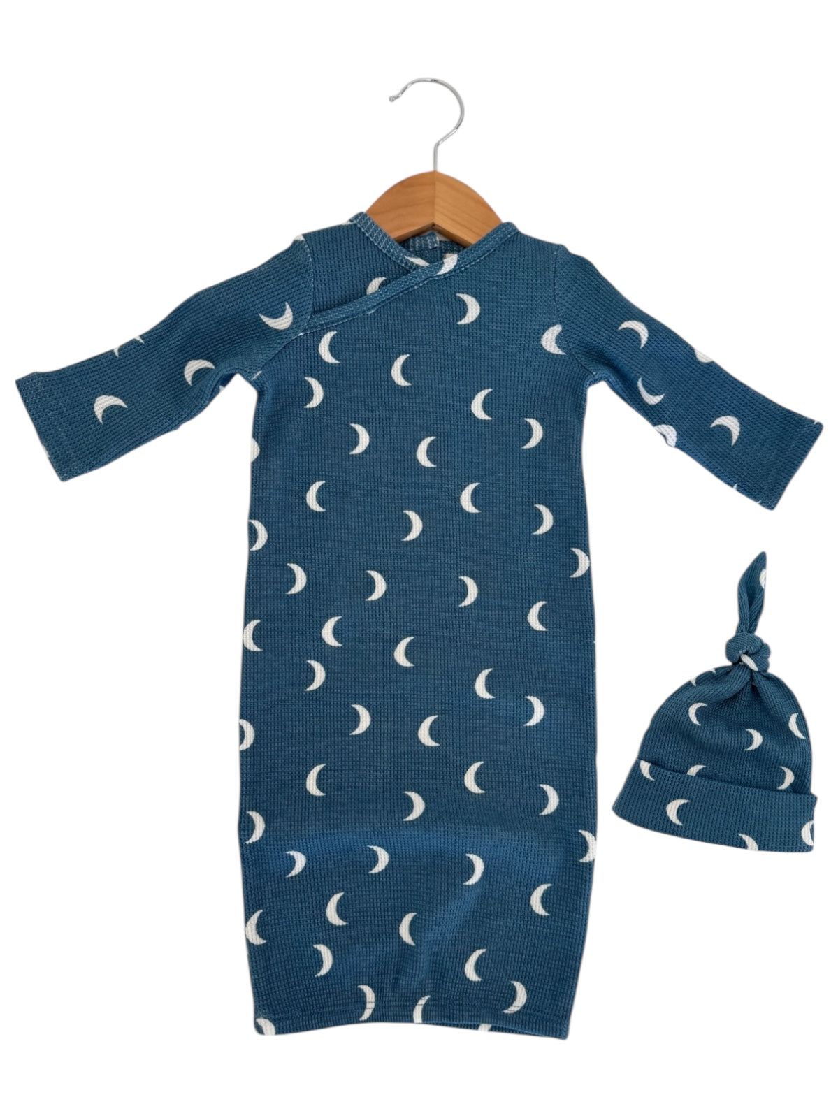 Blue baby gown with white crescent moon patterns, paired with a matching knot hat, hanging on a wooden hanger.