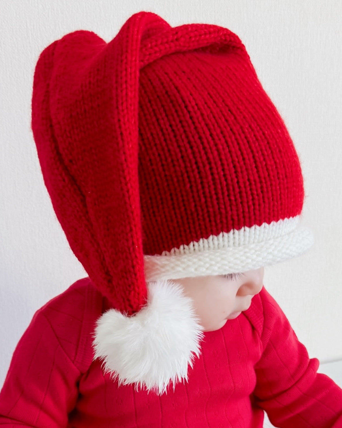 Child wearing a red festive Santa hat with a white pom-pom, dressed in a matching red sweater.