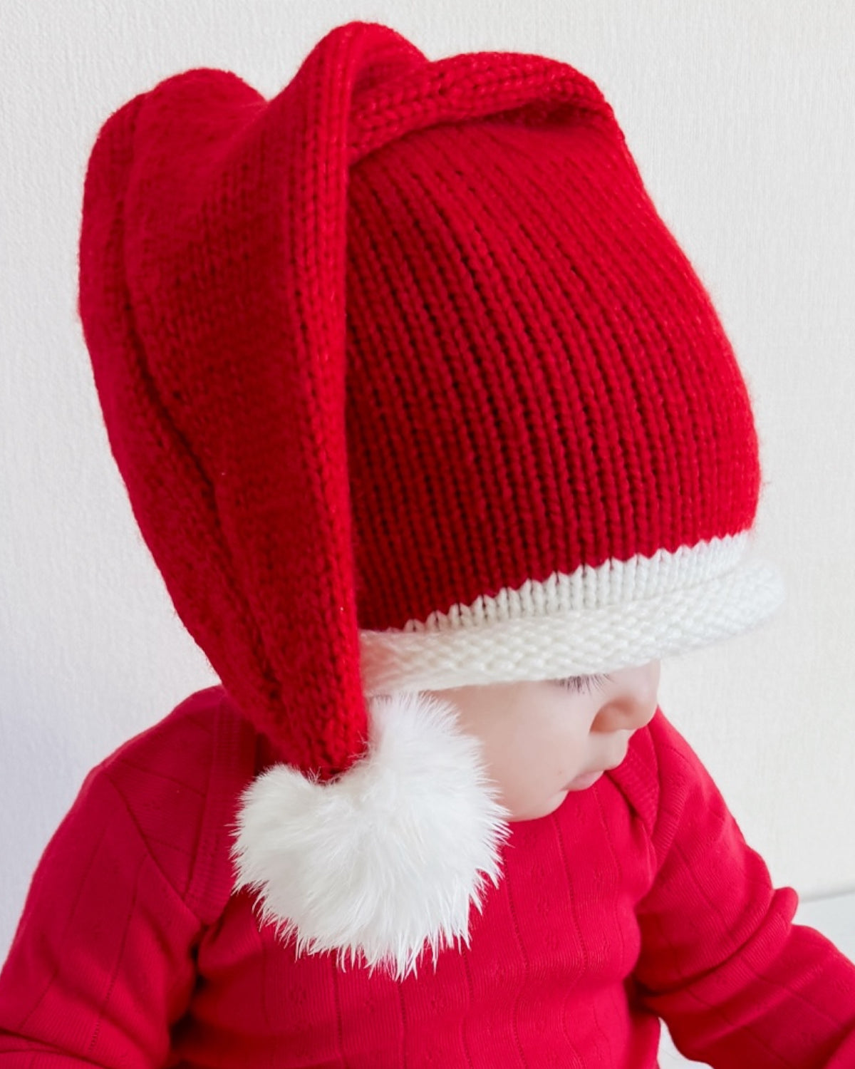 Child wearing a red festive Santa hat with a white pom-pom, dressed in a matching red sweater.