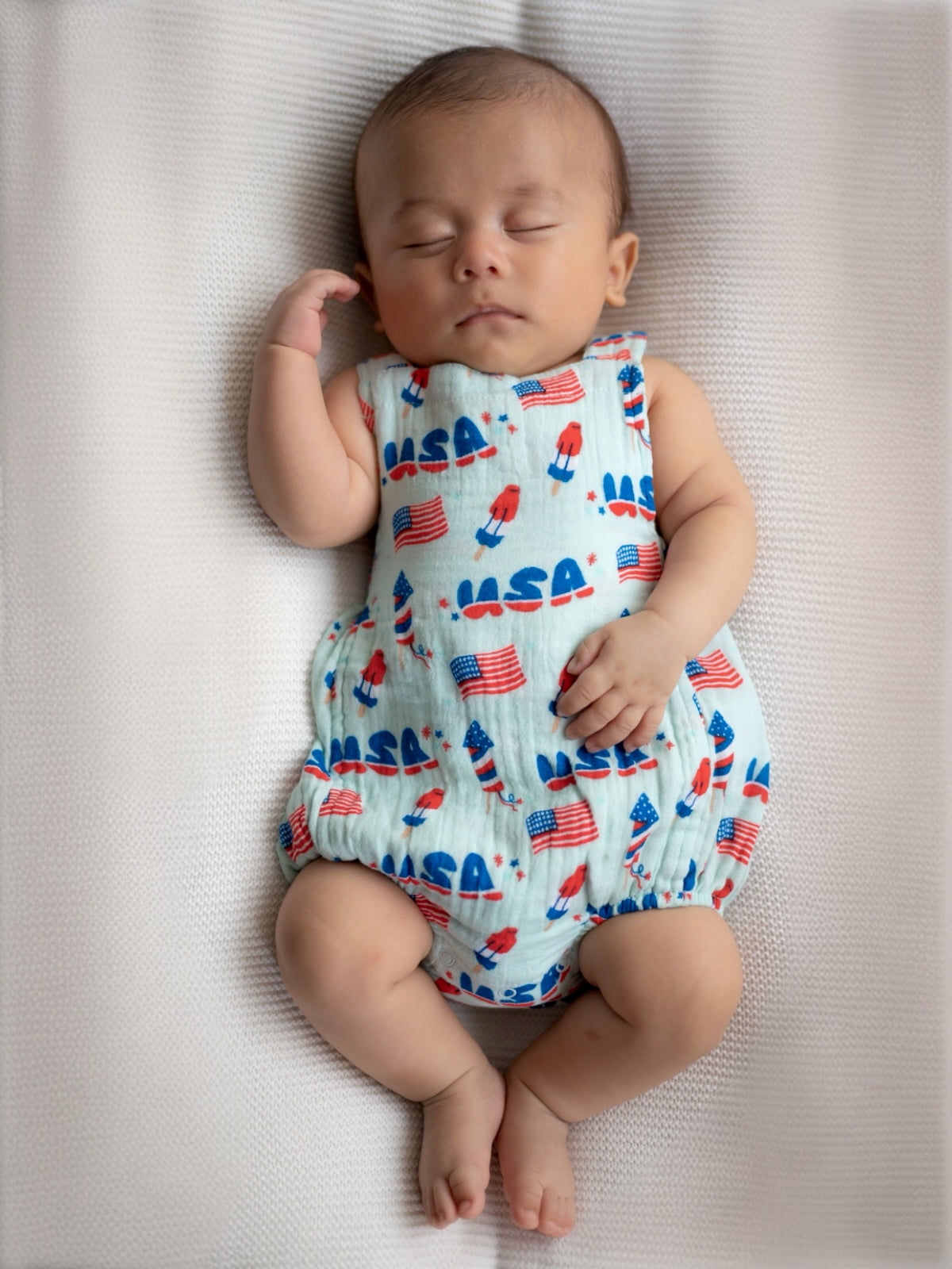 Baby wearing a USA-themed outfit, peacefully sleeping on a textured blanket.