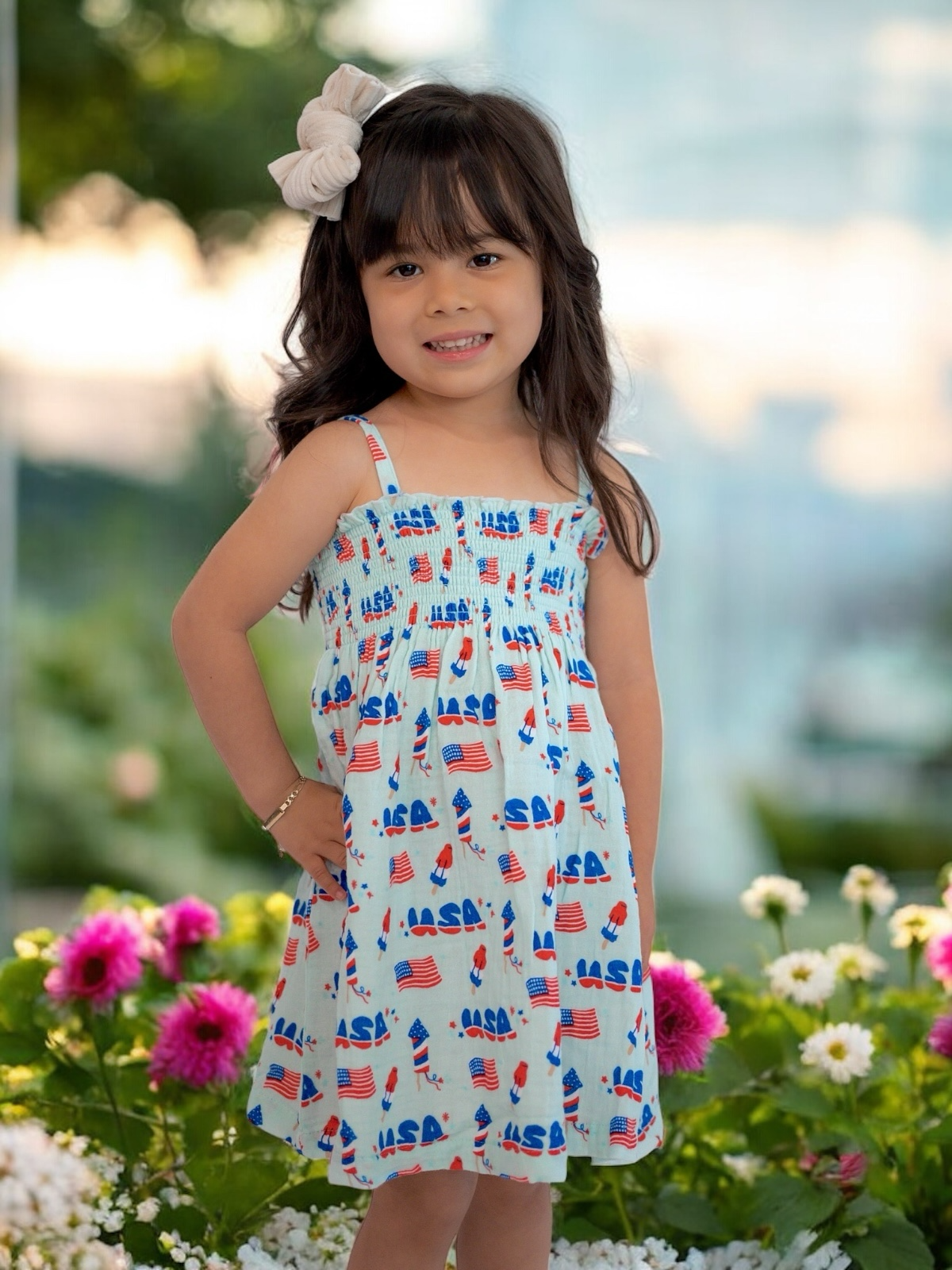 Smiling girl in a USA-themed dress poses among colorful flowers, showcasing a joyful and playful atmosphere.