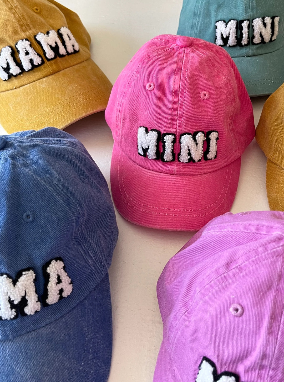 Colorful hats with “MAMA” and “MINI” text, arranged on a white surface.
