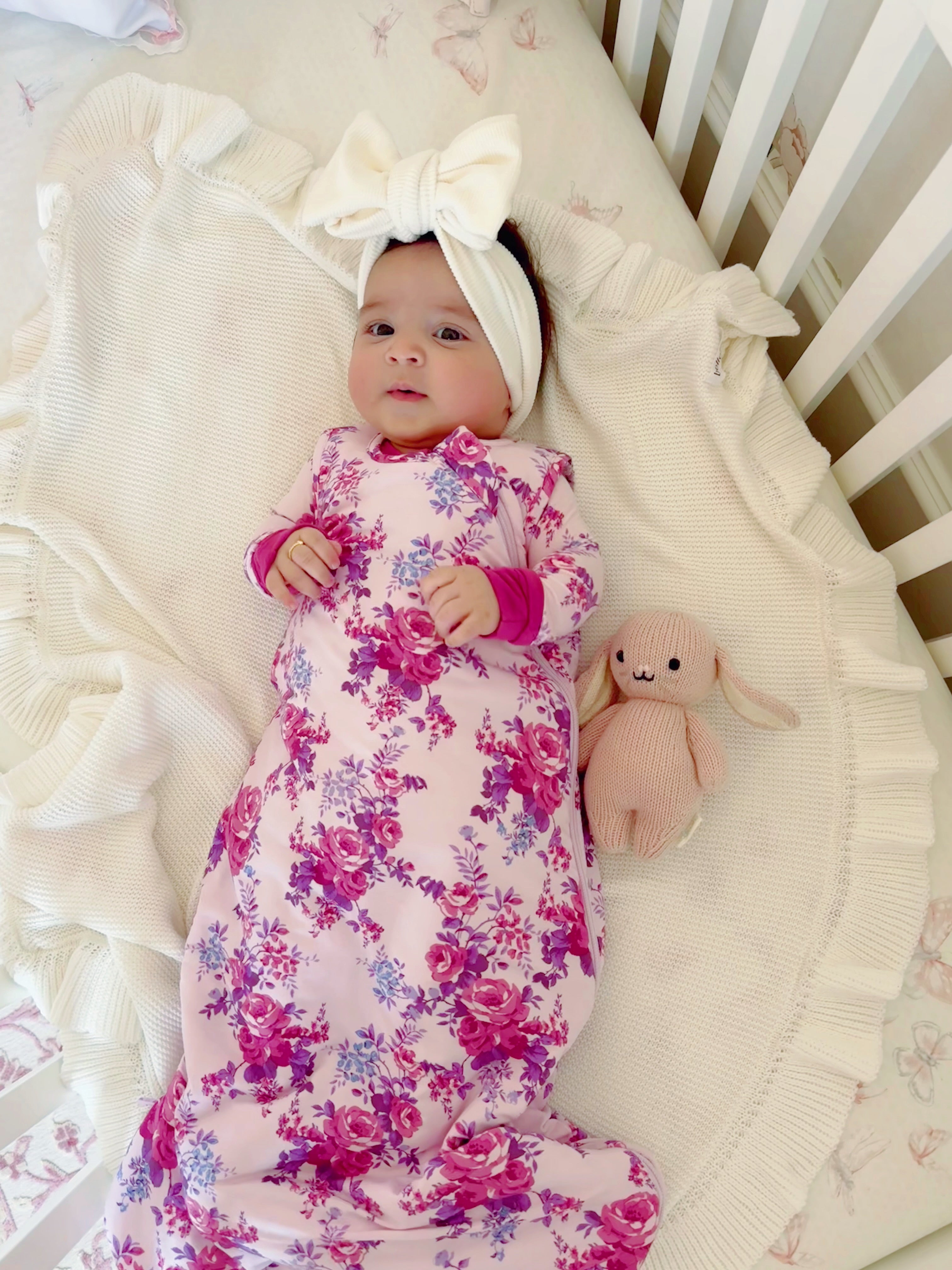 Infant in floral swaddle on a blanket, wearing a headband, with a plush bunny stuffed toy nearby.