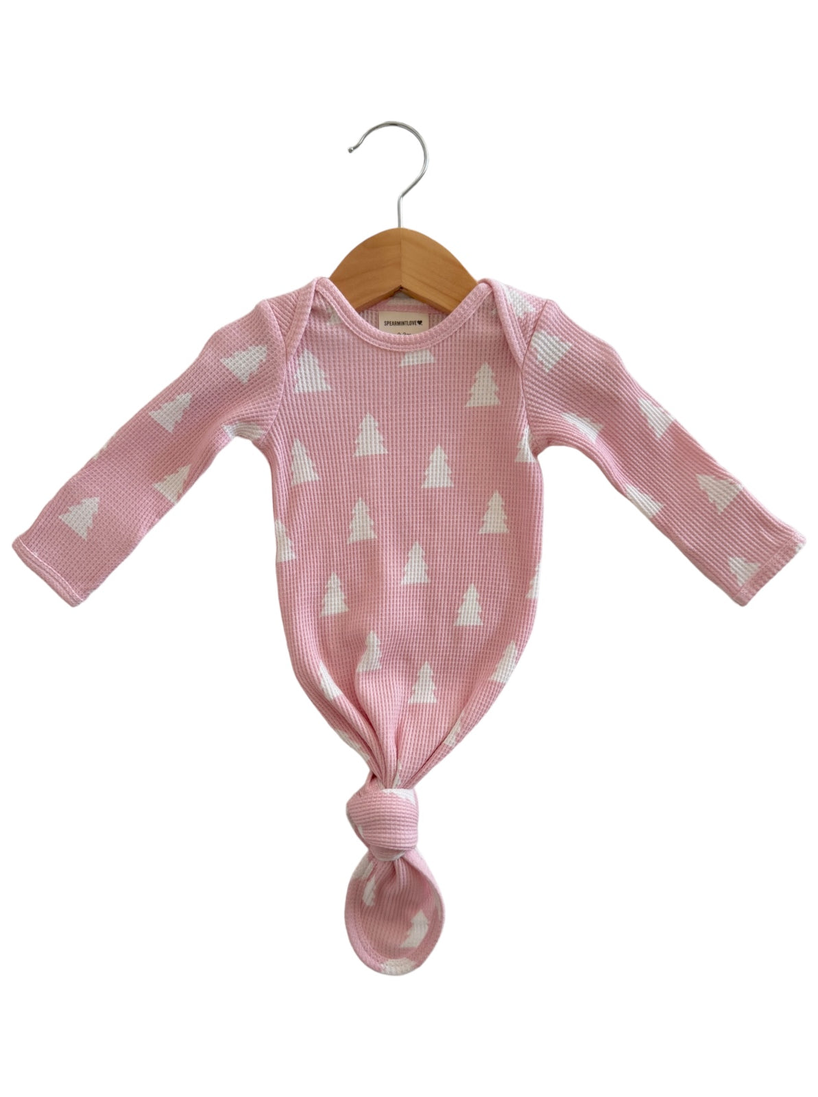 Pink newborn gown with white tree patterns, tied at the bottom, displayed on a wooden hanger.