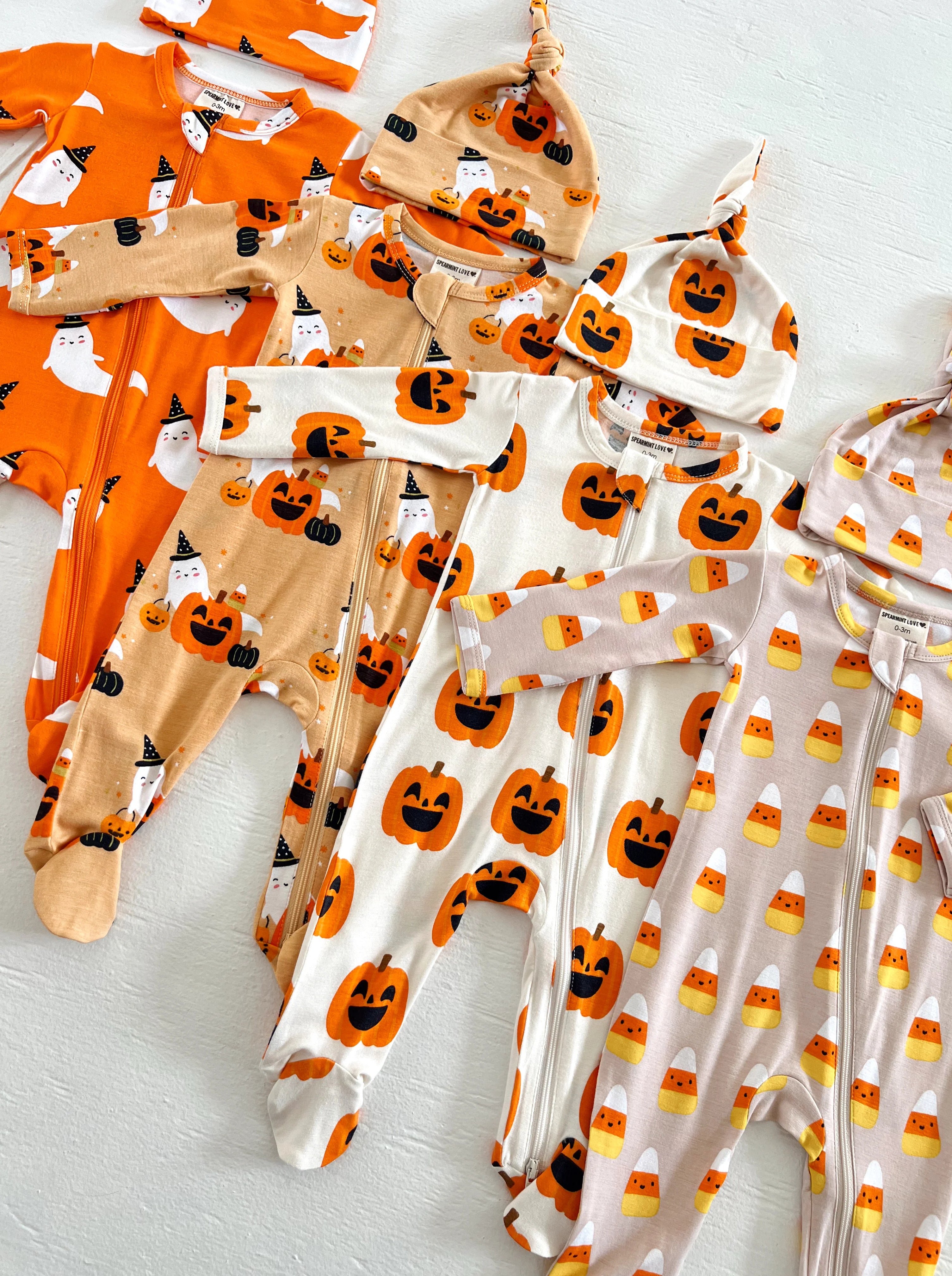 Assorted Halloween-themed baby outfits and hats in pumpkin and ghost designs arranged neatly on a white surface.
