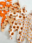 Assorted Halloween-themed baby outfits and hats in pumpkin and ghost designs arranged neatly on a white surface.