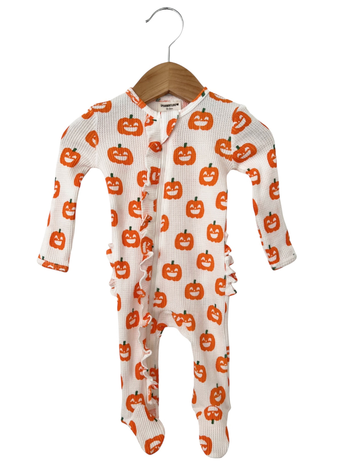 White onesie with orange pumpkin prints and ruffle details, hanging on a wooden hanger. Perfect for Halloween.