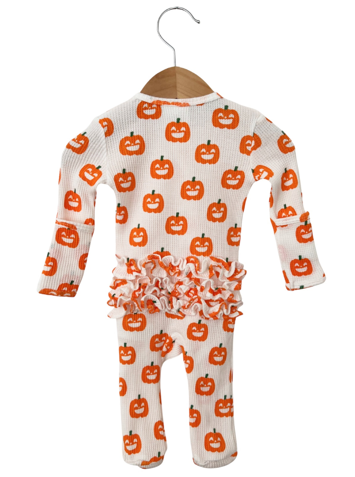 Infant pajama set featuring a pumpkin print and ruffled trim, hanging on a wooden hanger against a white background.