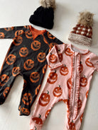 Two children's Halloween onesies with pumpkin designs and two knitted hats, one black and one brown checkered.