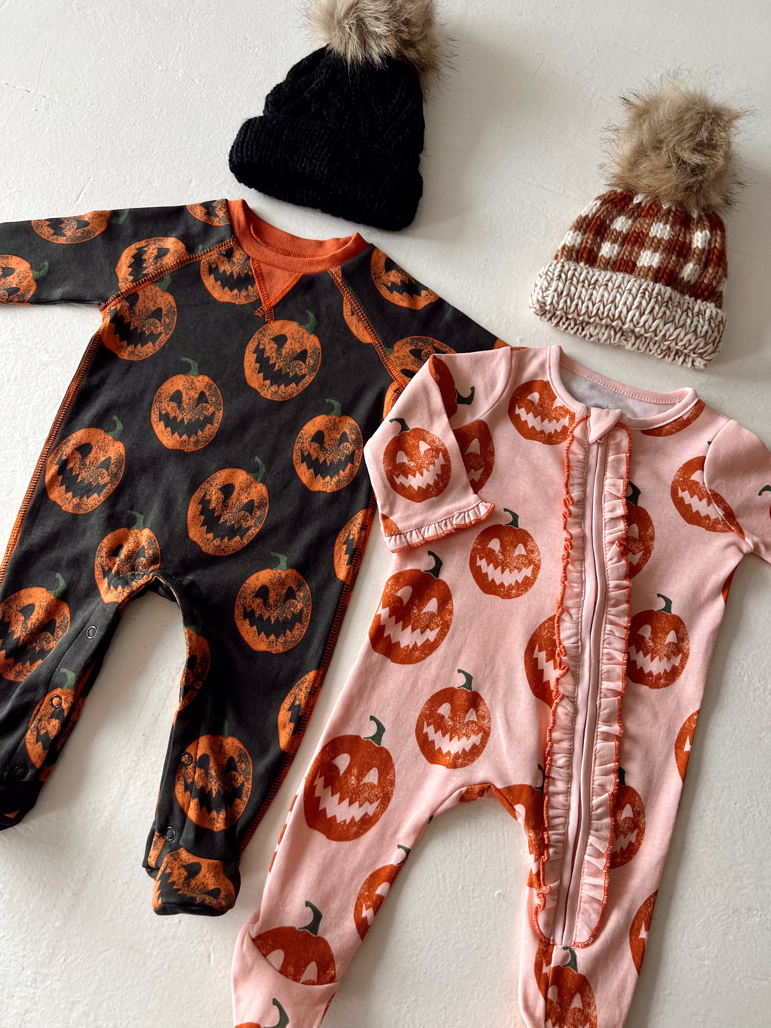 Two children's Halloween onesies with pumpkin designs and two knitted hats, one black and one brown checkered.