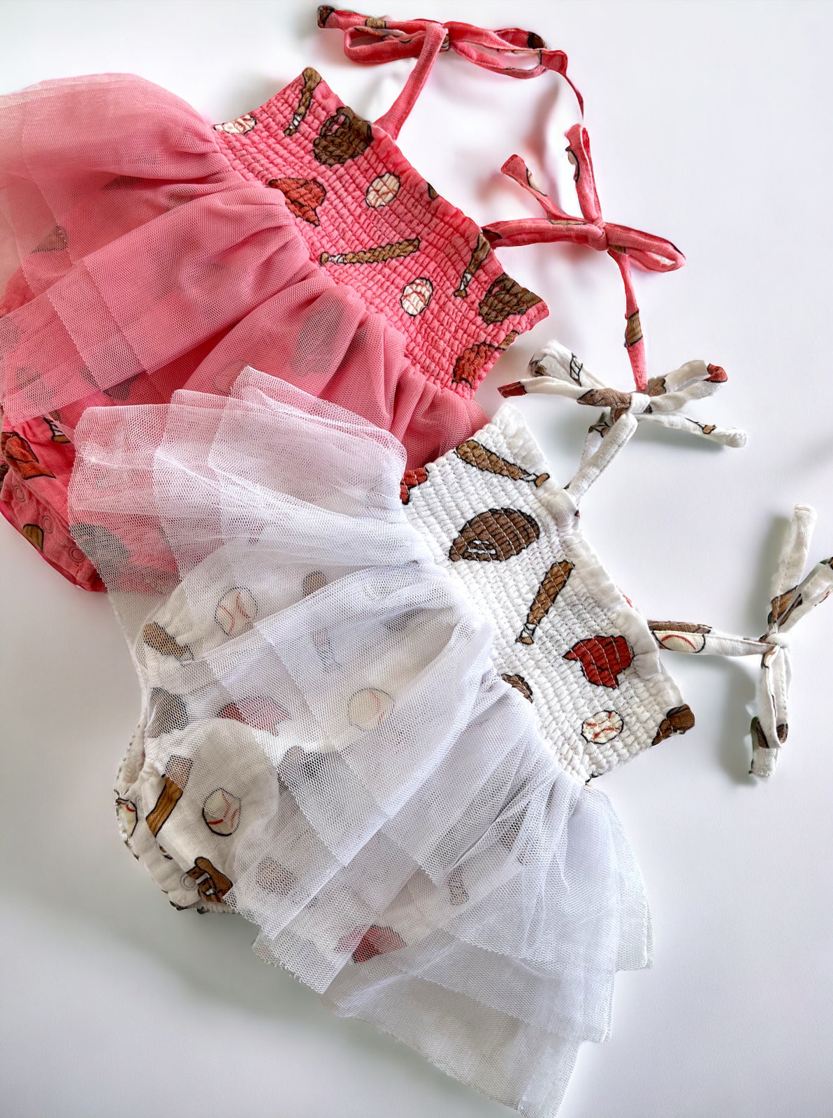Two colorful toddler dresses with sports and baseball motifs, one pink and one white, on a white background.
