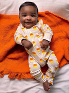 Smiling baby in candy corn pajamas on an orange blanket, relaxed and happy.