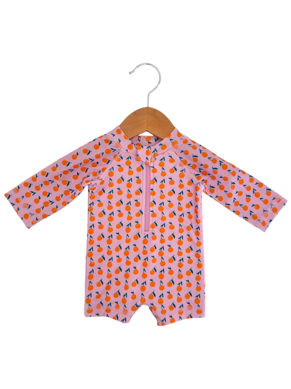 Pink children's rash guard with orange and blue fruit pattern, hanging on a wooden hanger.