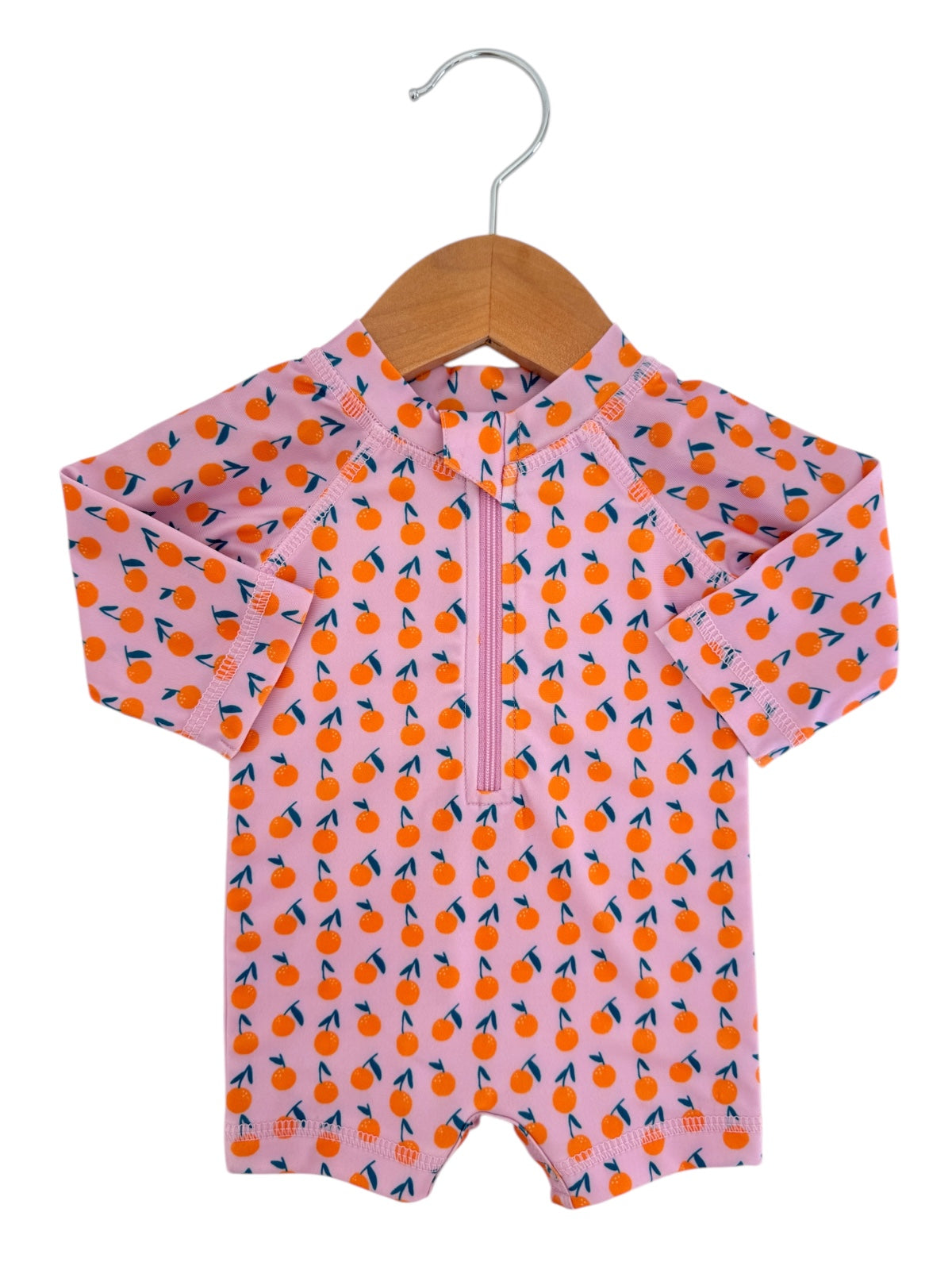 Pink long-sleeve swimsuit for kids with orange fruit pattern, displayed on a wooden hanger.