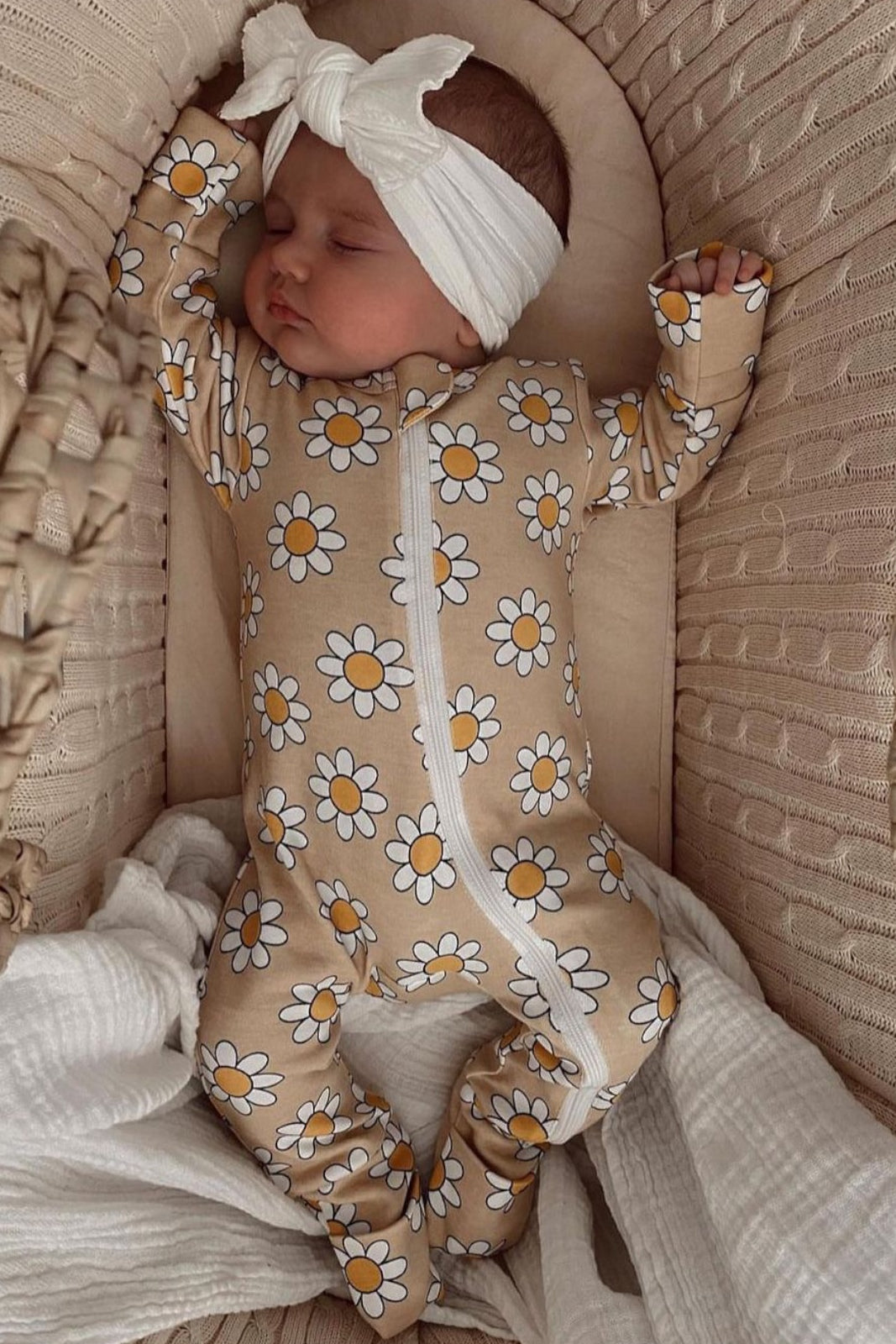Baby sleeping in a floral onesie and headband, nestled in a cozy basket with soft fabrics.