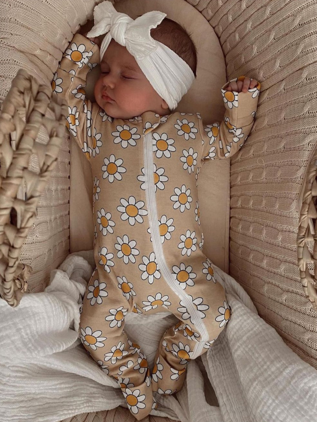Baby sleeping in a floral onesie and headband, nestled in a cozy basket with soft fabrics.