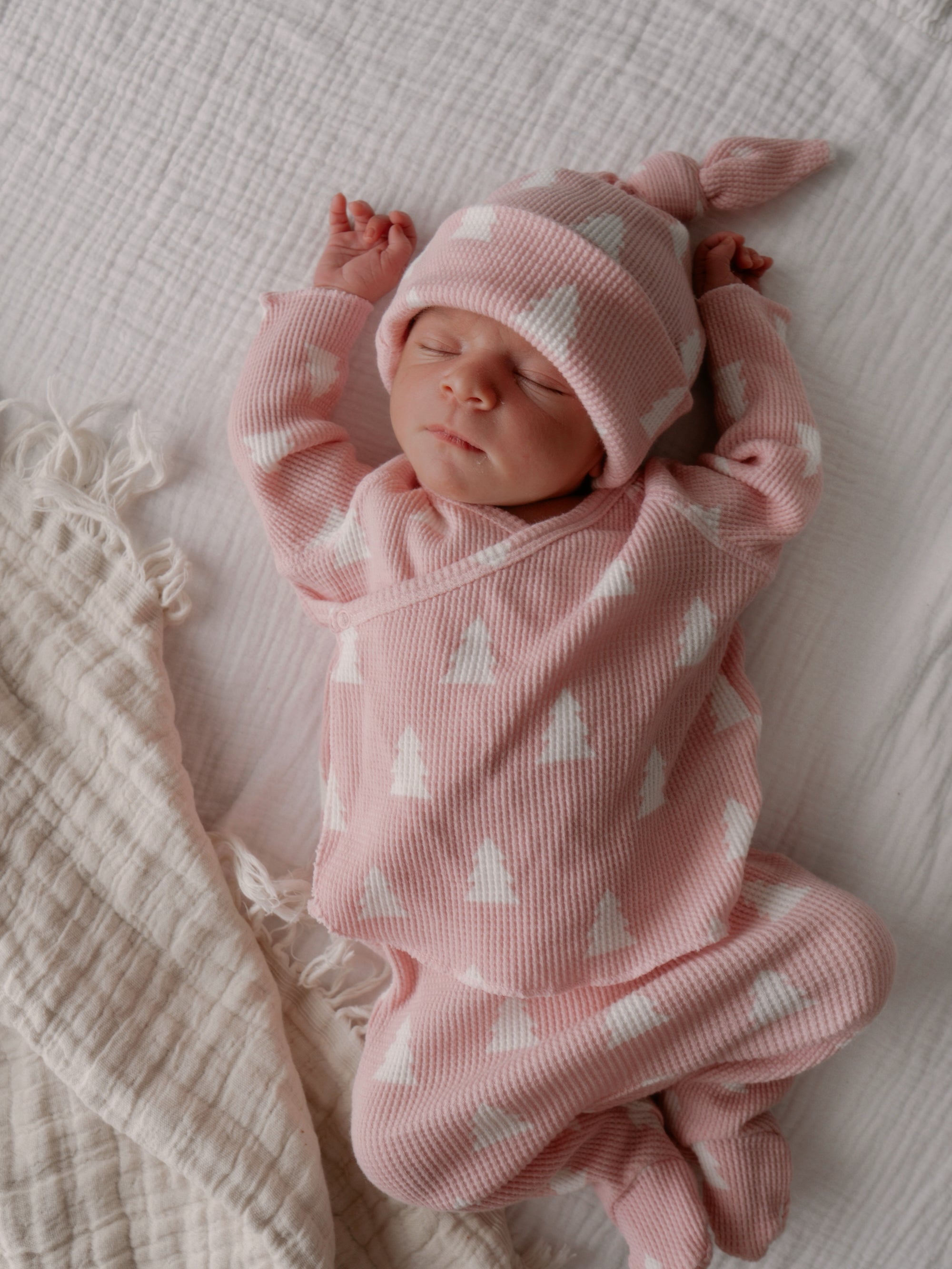 Newborn baby in pink outfit with white patterns, resting peacefully on a soft blanket.