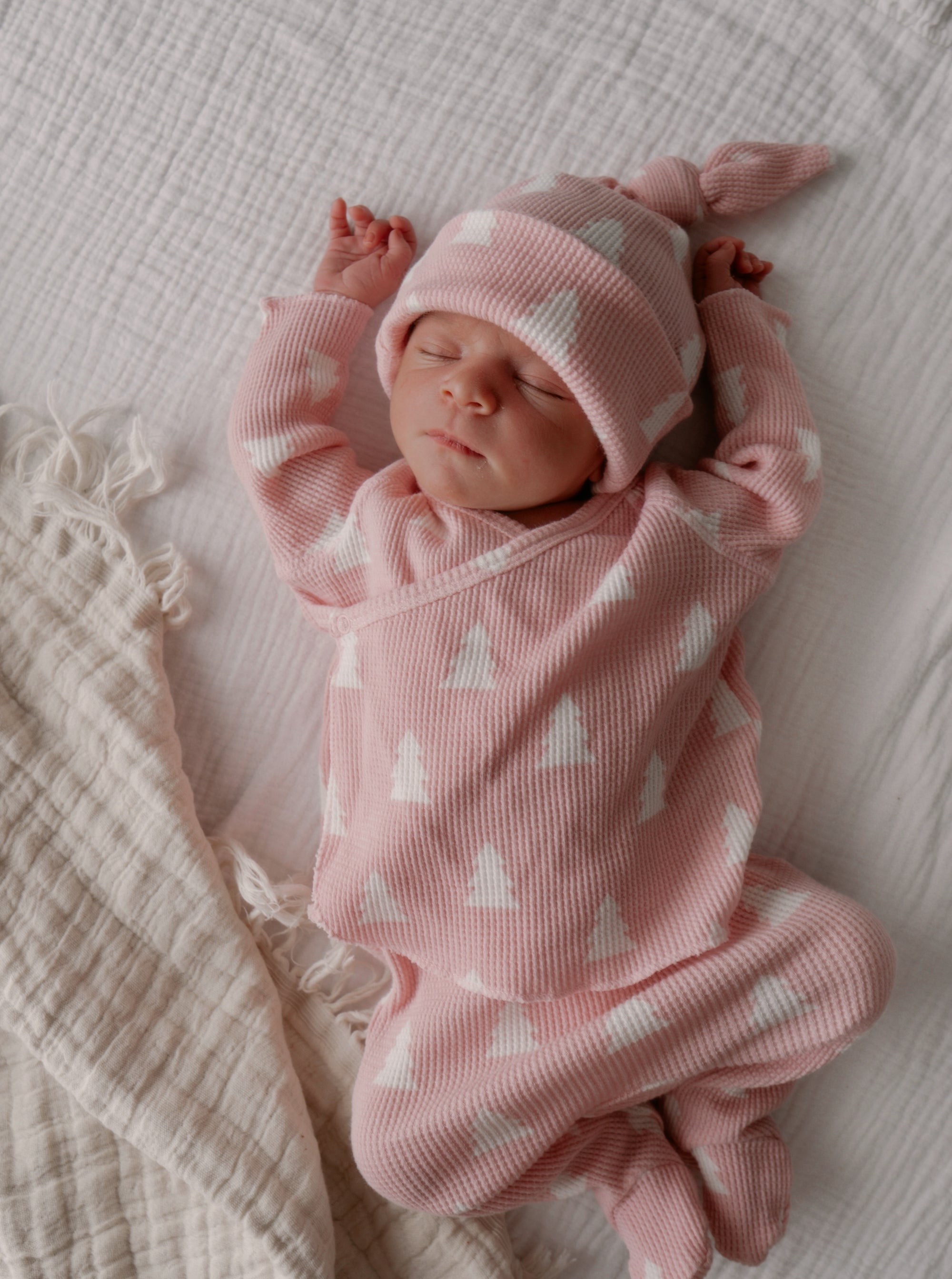 Newborn baby in pink outfit with white patterns, resting peacefully on a soft blanket.