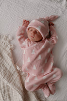 Newborn baby in pink outfit with white patterns, resting peacefully on a soft blanket.