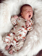 Baby in a snowman-patterned outfit yawning on a fluffy white rug.