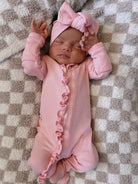 Infant girl in a pink onesie and bow sleeping on a checkered blanket.
