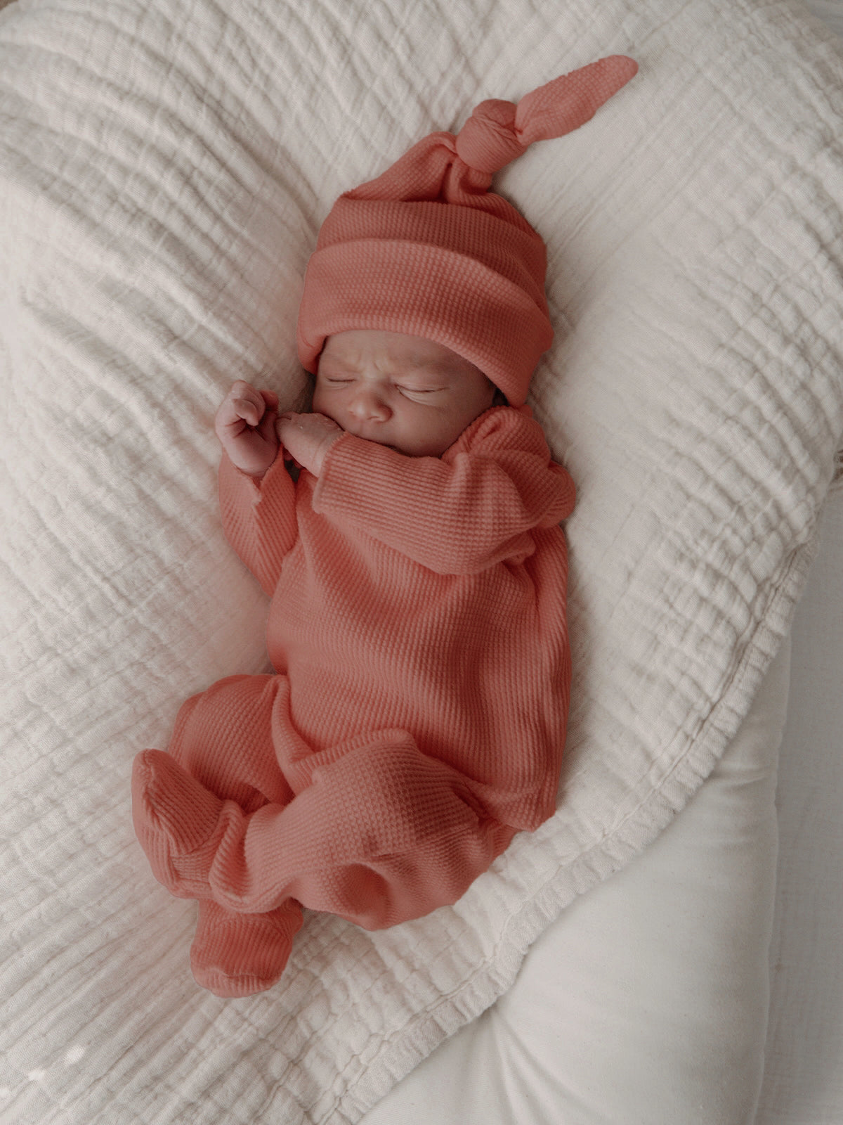 Newborn baby sleeping on a cozy blanket, wearing a rust-colored outfit and matching hat.