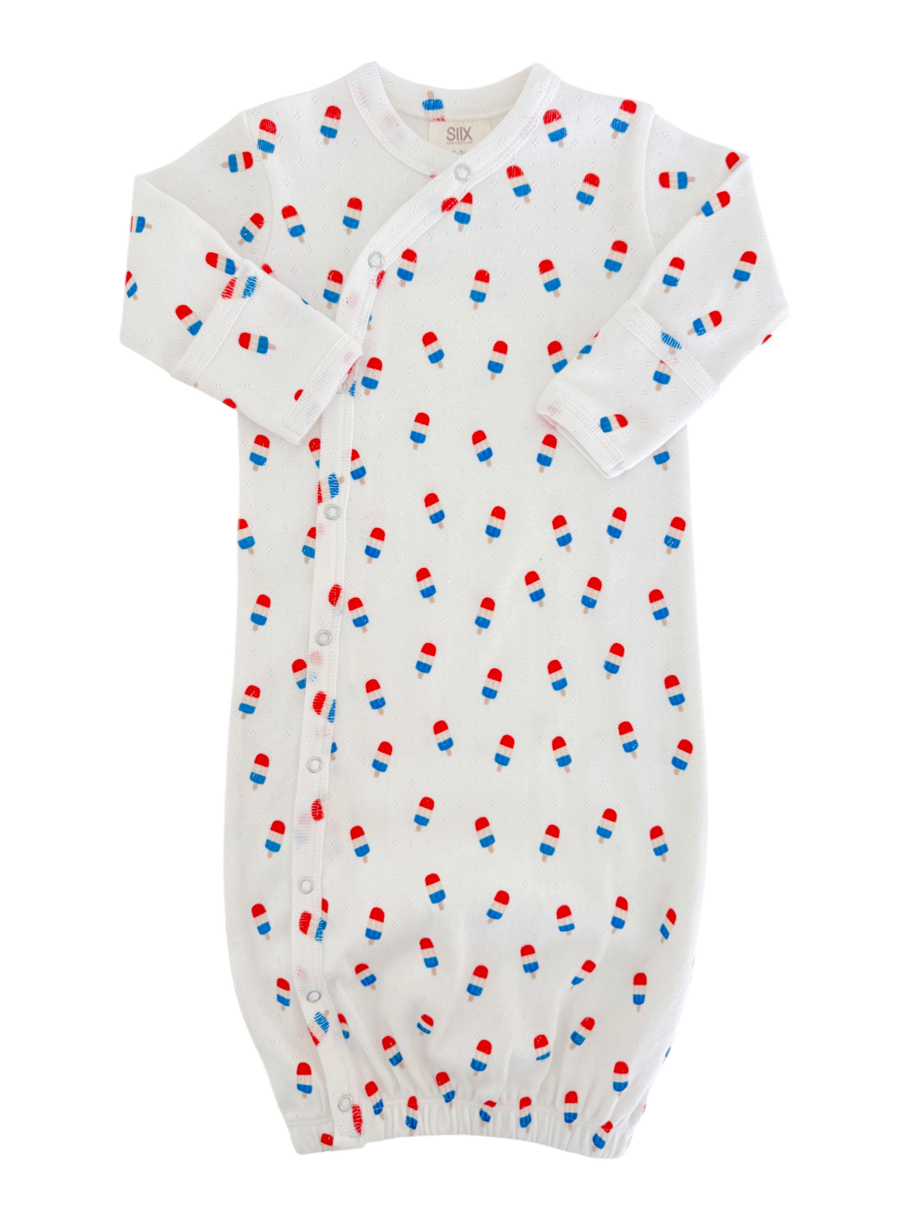 White baby gown with red and blue pill patterns, featuring long sleeves and snap buttons down the side.