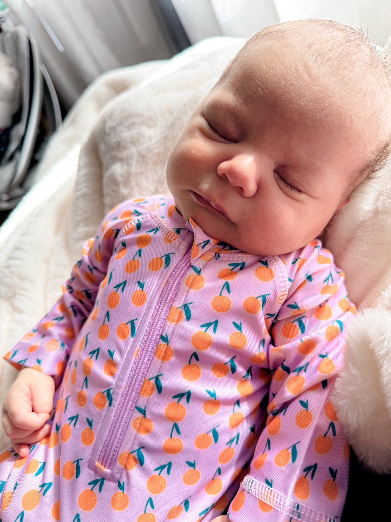 Baby sleeping peacefully in a colorful orange-patterned onesie on a soft, cozy blanket.