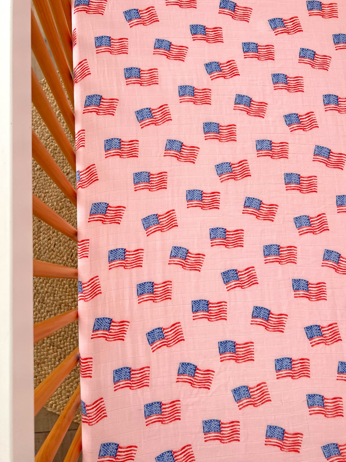 Pink crib sheet featuring a repeated pattern of small American flags.