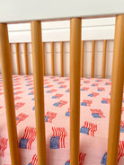 Crib with wooden slats and pink fabric featuring a repeated American flag pattern.